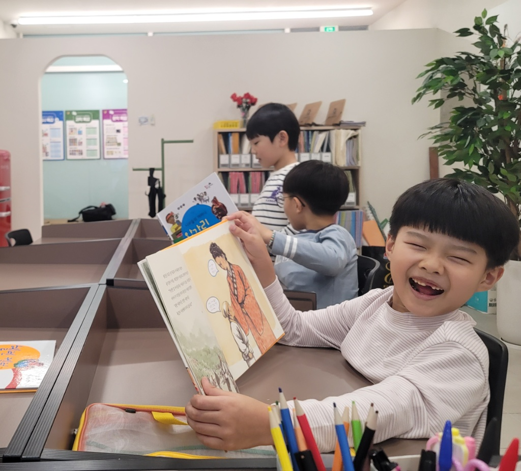 친구들과 책을 보며 밝게 웃는 다글 학생