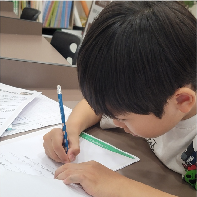 다글 교실에서 연필로 자신의 생각을 글로 쓰는 아이